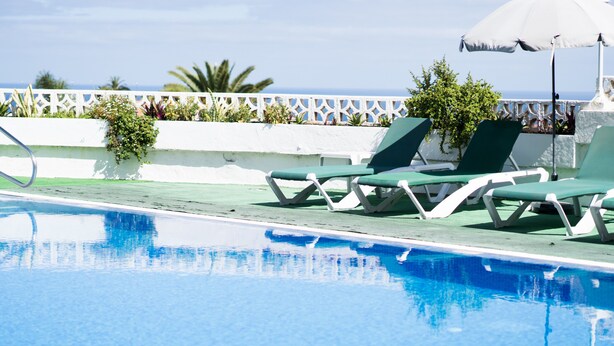 Una piscina con agua cristalina azul, rodeada de barandas blancas y sillones reclinables verdes.