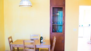 Una mesa de comedor con sillas, una botella de vino y vasos. Detrás de la mesa hay un mueble de madera con puertas de cristal.