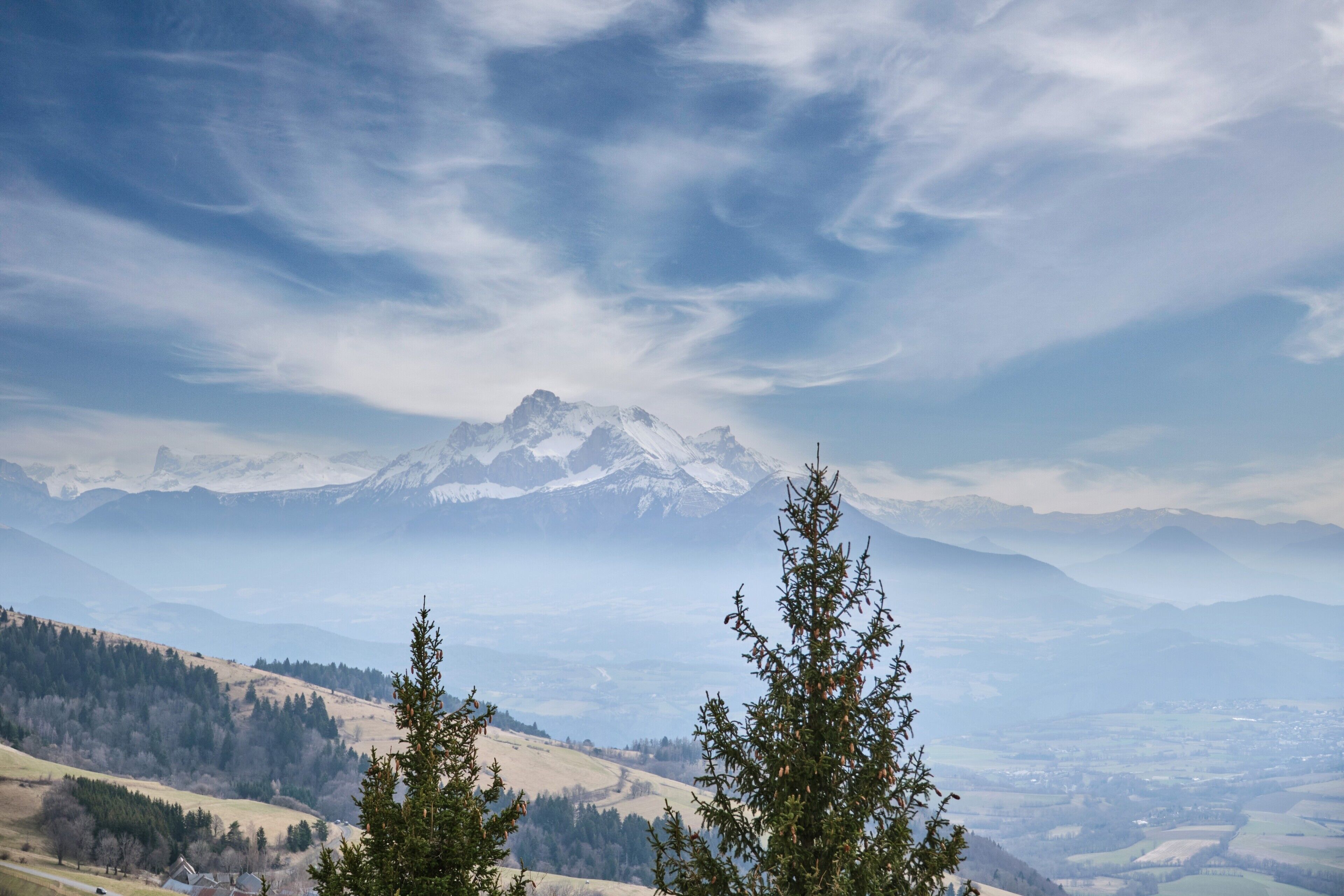 Eine Berglandschaft mit schneebedeckten Gipfeln, immergrünen Bäumen und einem Tal.