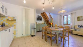 A spacious kitchen with a dining area, a staircase, and a living room with a sofa and a window.