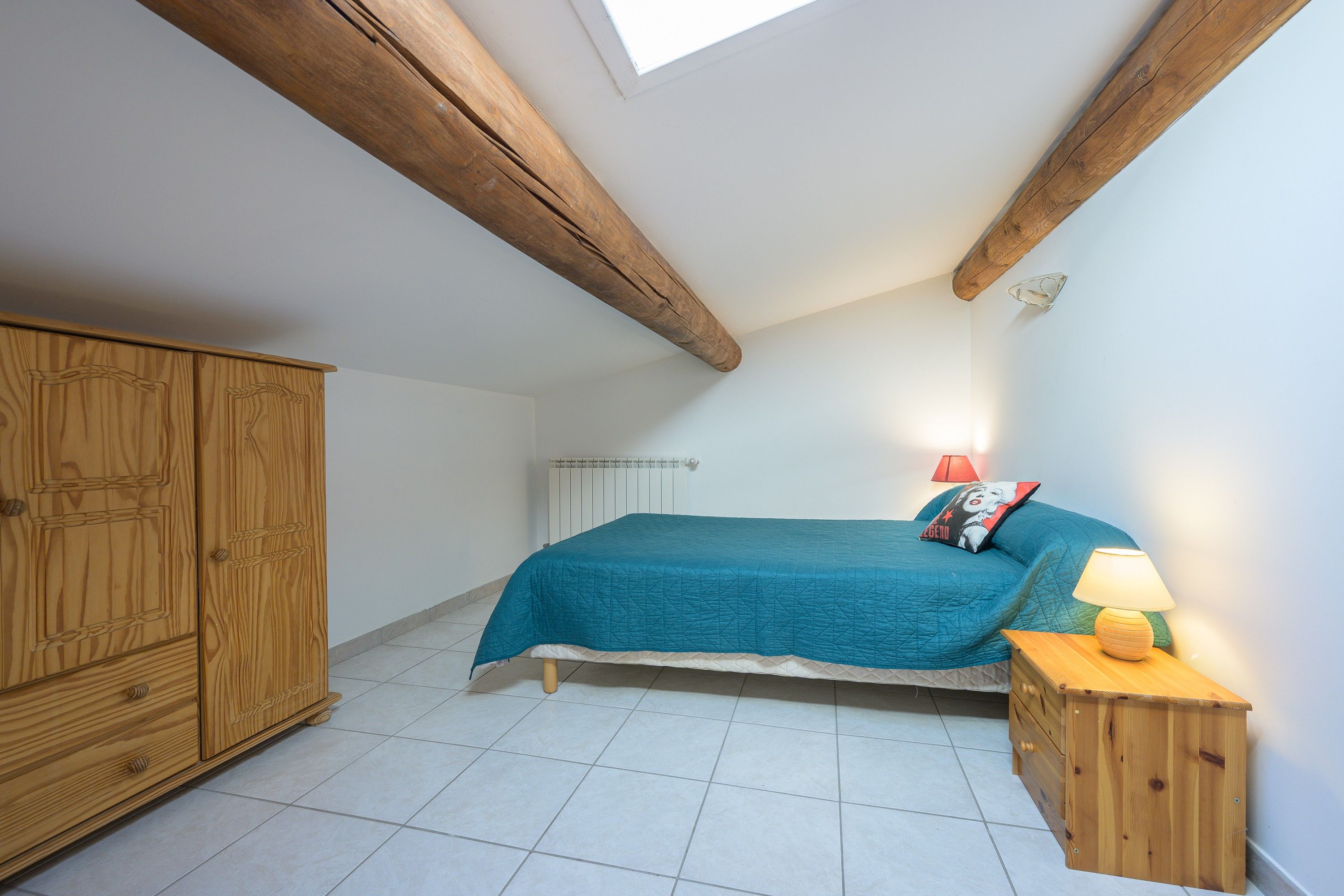Une chambre à coucher avec un lit, une armoire en bois, un radiateur et une table de chevet avec une lampe.