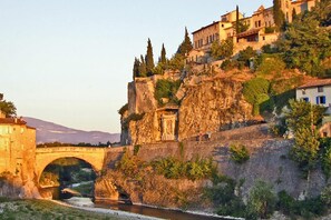 A stone bridge over a river, a historic building with a stone facade, and a hillside with residential buildings.