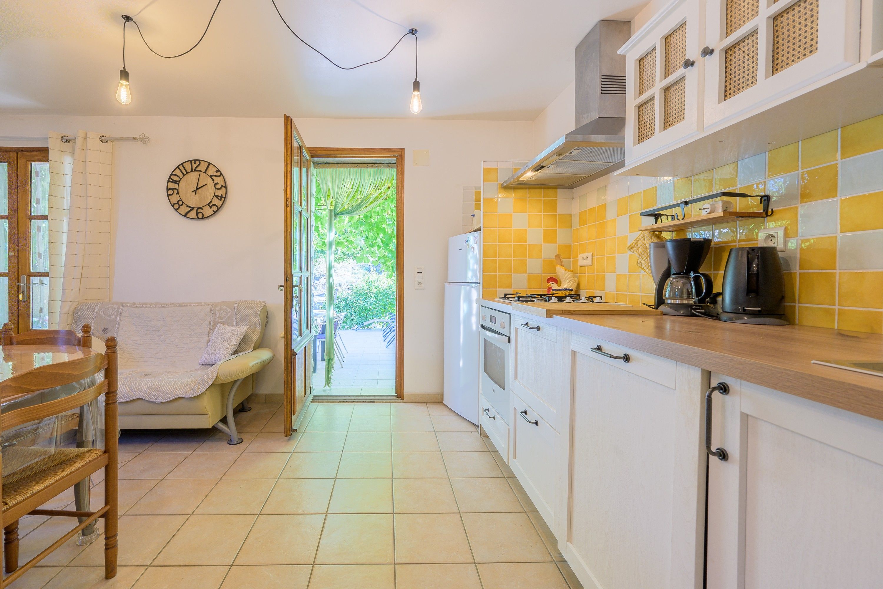 A kitchen with a dining area, a clock on the wall, and a view through an open door.
