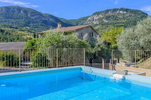 A swimming pool with a stone house in the background, surrounded by trees and mountains.