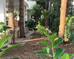 A garden area with trees, a pathway, and a building in the background. - Villa Dyrrahu (Golem)