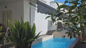 A swimming pool with a tiled edge, surrounded by potted plants and a white building with a covered patio. - Villa Dyrrahu (Golem)