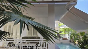 A covered outdoor area with a pool, white railing, and potted plants.