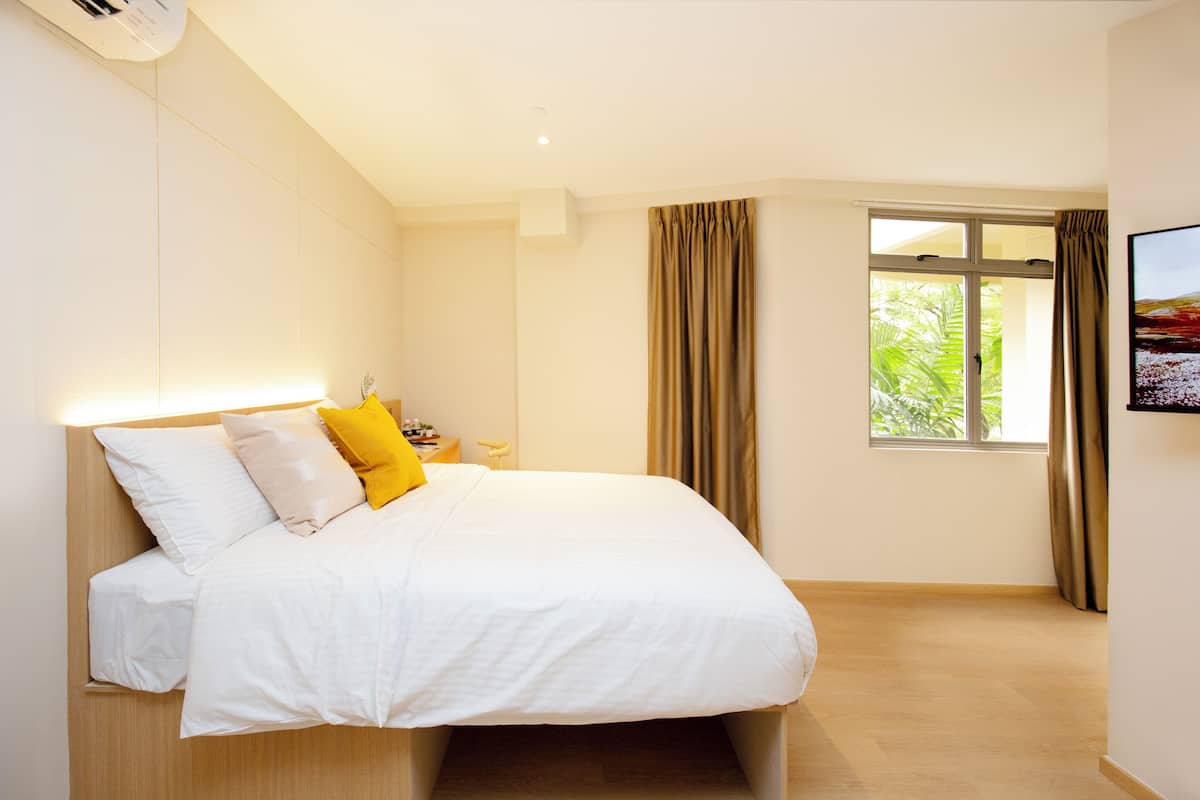 A modern hotel room with a large bed, a bedside table, a window with curtains, and a painting on the wall.