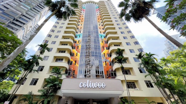 A high-rise hotel with a central glass elevator shaft, multiple balconies, and palm trees around. - Coliwoo Orchard (Singapore)