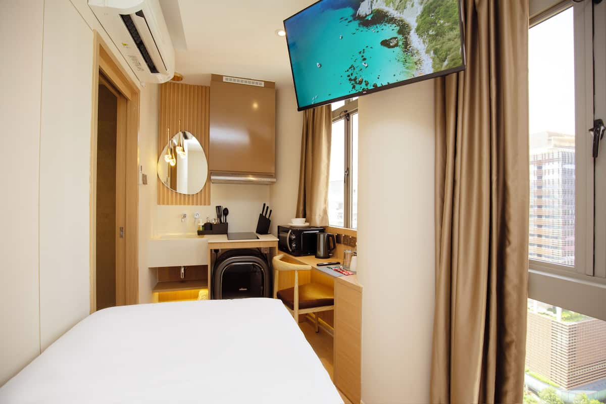 A hotel room with a bed, a desk with a microwave, a sink, and a TV mounted on the wall.