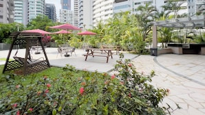 A rooftop garden with outdoor seating, surrounded by tall buildings. - Coliwoo Orchard (Singapore)