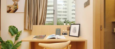 Habitación de hotel con un escritorio de madera, una silla, una planta en maceta, una ventana con cortinas y un cuadro de un ciervo en la pared.