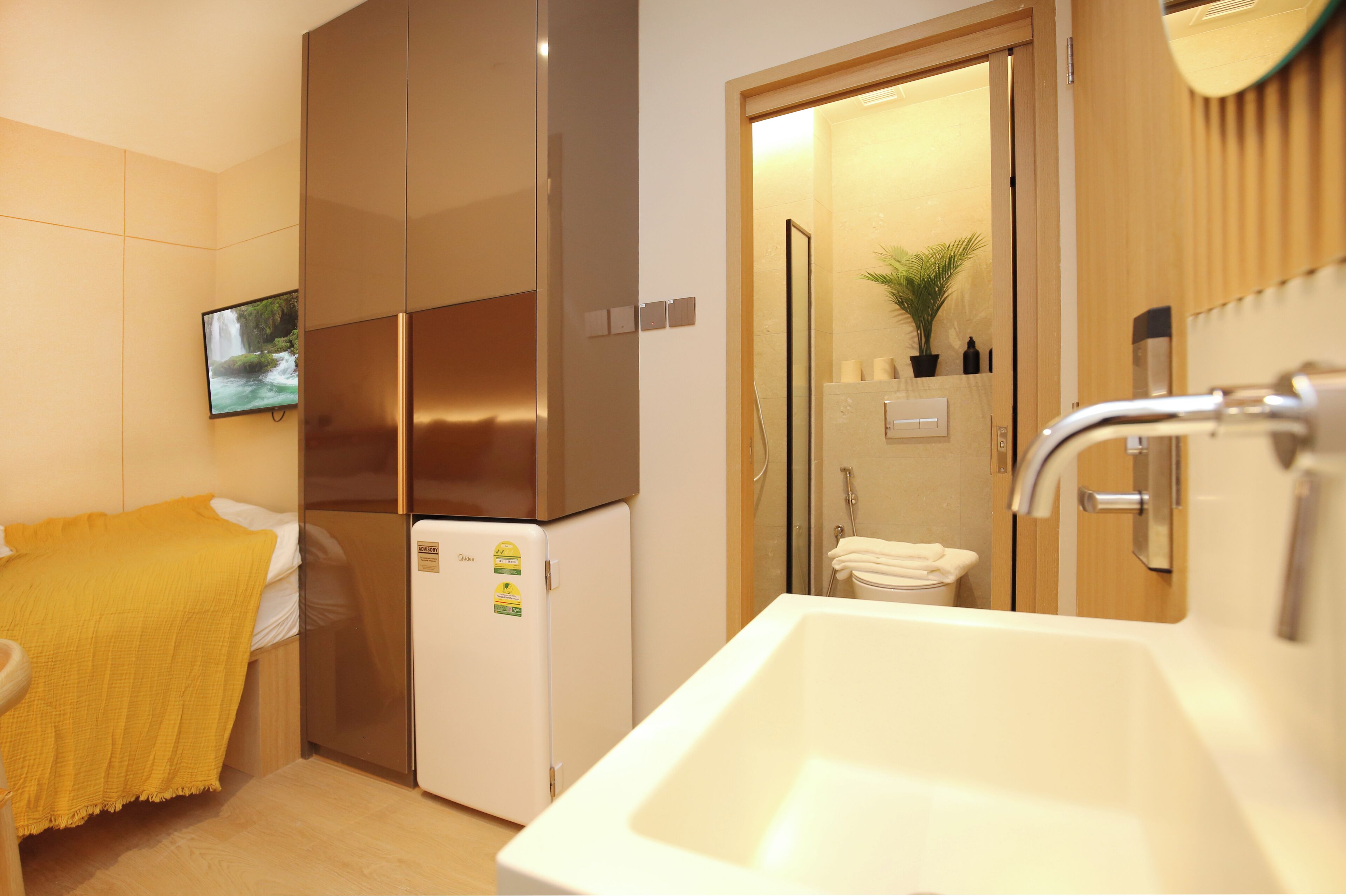 A compact hotel room with a bed, a small refrigerator, a sink, and a shower area.