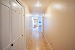 A hallway with wooden flooring and white walls, leading to a kitchen area with cabinets and a countertop.