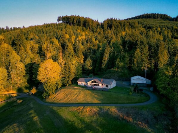 A two-story house with a large front porch, surrounded by a forested area.
