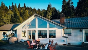 Ein Haus mit großen Fenstern, einer überdachten Terrasse und einer Feuerstelle.