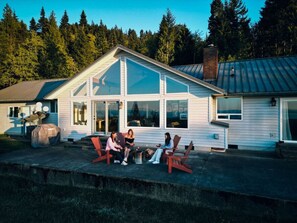 A house with a large glass front, a covered grill, and outdoor seating.