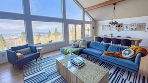 Ein modernes Wohnzimmer mit großem Fenster, einem blauen Sofa, einem Couchtisch und Blick ins Freie.