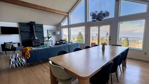 Eine moderne Küche mit einer großen Kochinsel, ein Essbereich mit einem Holztisch und Stühlen sowie Bergblick durch große Fenster.