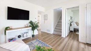 A modern living room with a flat-screen TV, a wooden console table, a potted plant, and a patterned rug.