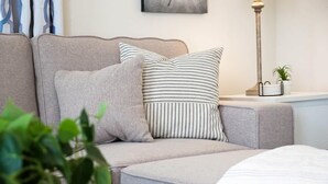 A modern living room with a sofa, striped pillows, a small table with a plant, and a lamp.