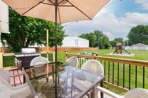 Une terrasse extérieure avec une table en verre, des chaises et un barbecue.