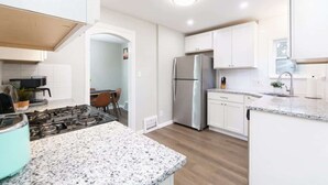 A modern kitchen with white cabinets, a stainless steel refrigerator, a gas stove, and a granite countertop. - Park-side family retreat with private backyard (University Heights)