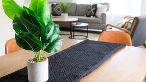 A dining table with a potted plant, a dark textured placemat, and a grey sofa in the background. - Park-side family retreat with private backyard (University Heights)