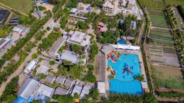 An aerial view of a residential area with a swimming pool, houses, and a road. - Longquan Xiangyuan Shared Farm (Wenchang)