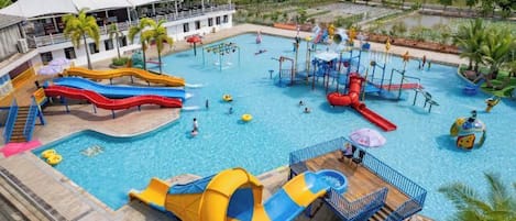 Un parc aquatique doté de nombreux toboggans et de plusieurs piscines, entouré d’un bâtiment surmonté de toits blancs en forme de parasol.