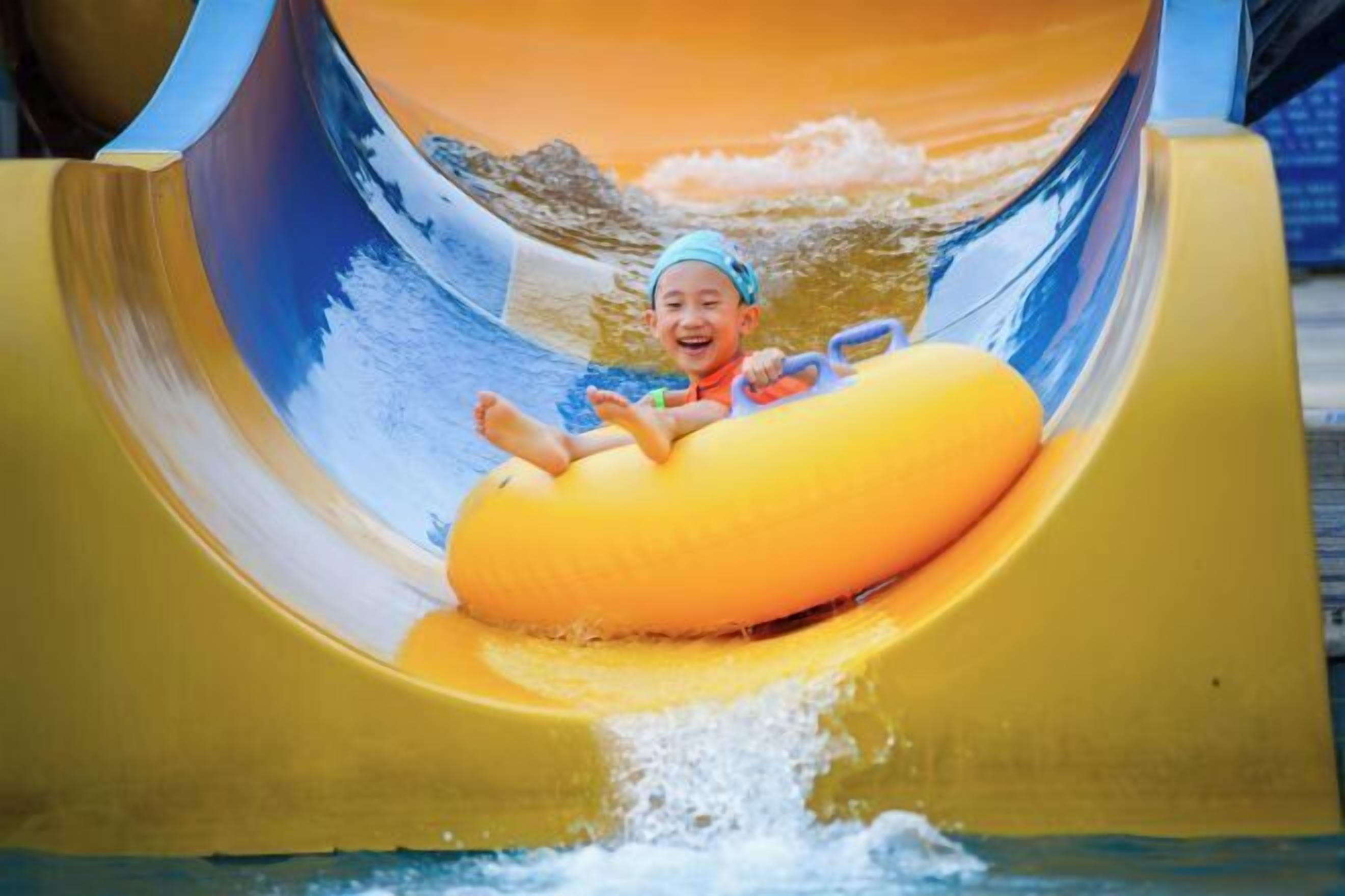 A child on a yellow water slide with a wave background.