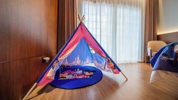 A room with a large window, a bed with a blue blanket, and a tent-like structure with Mickey Mouse on the floor.