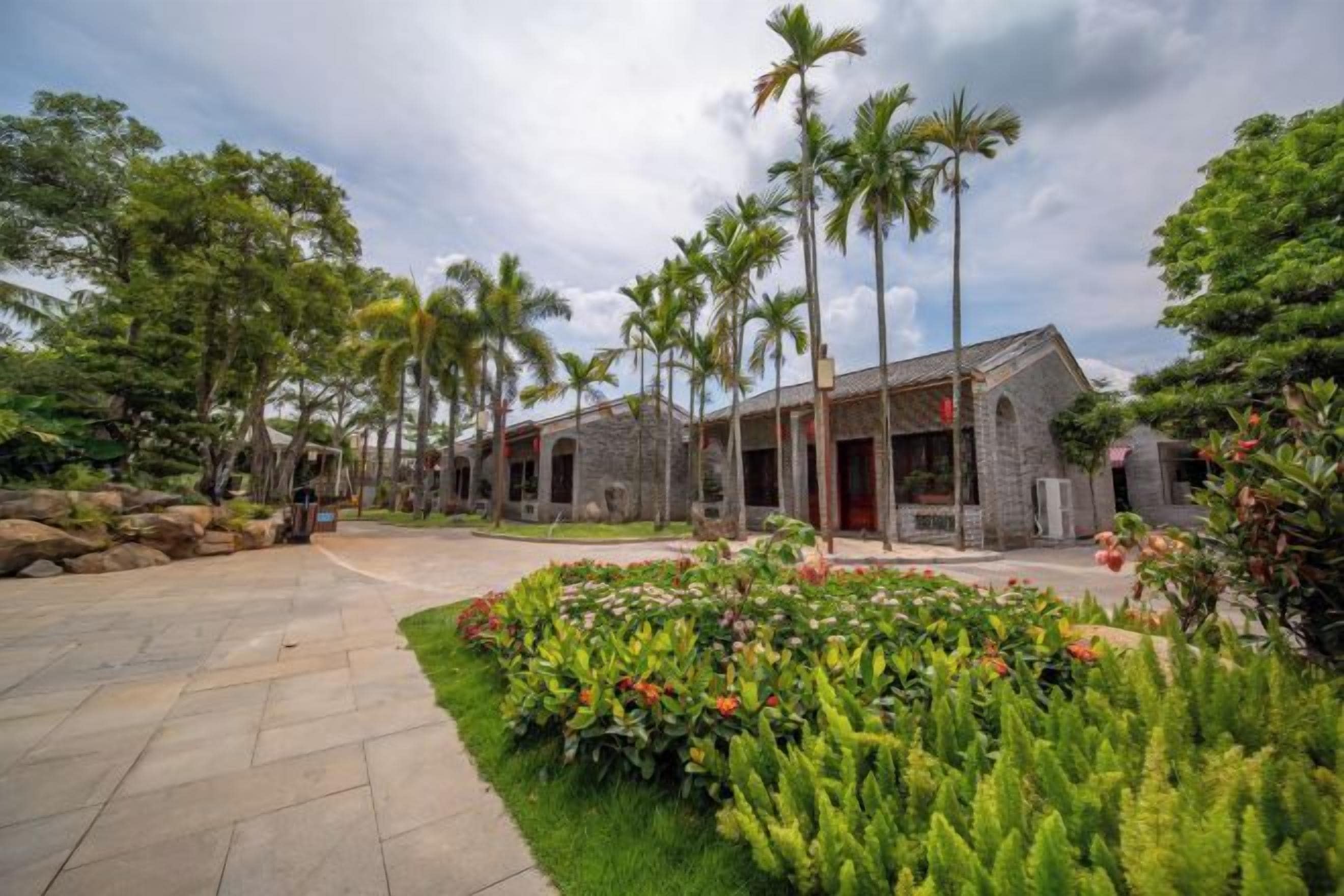 A building with a stone facade, surrounded by lush greenery and palm trees.