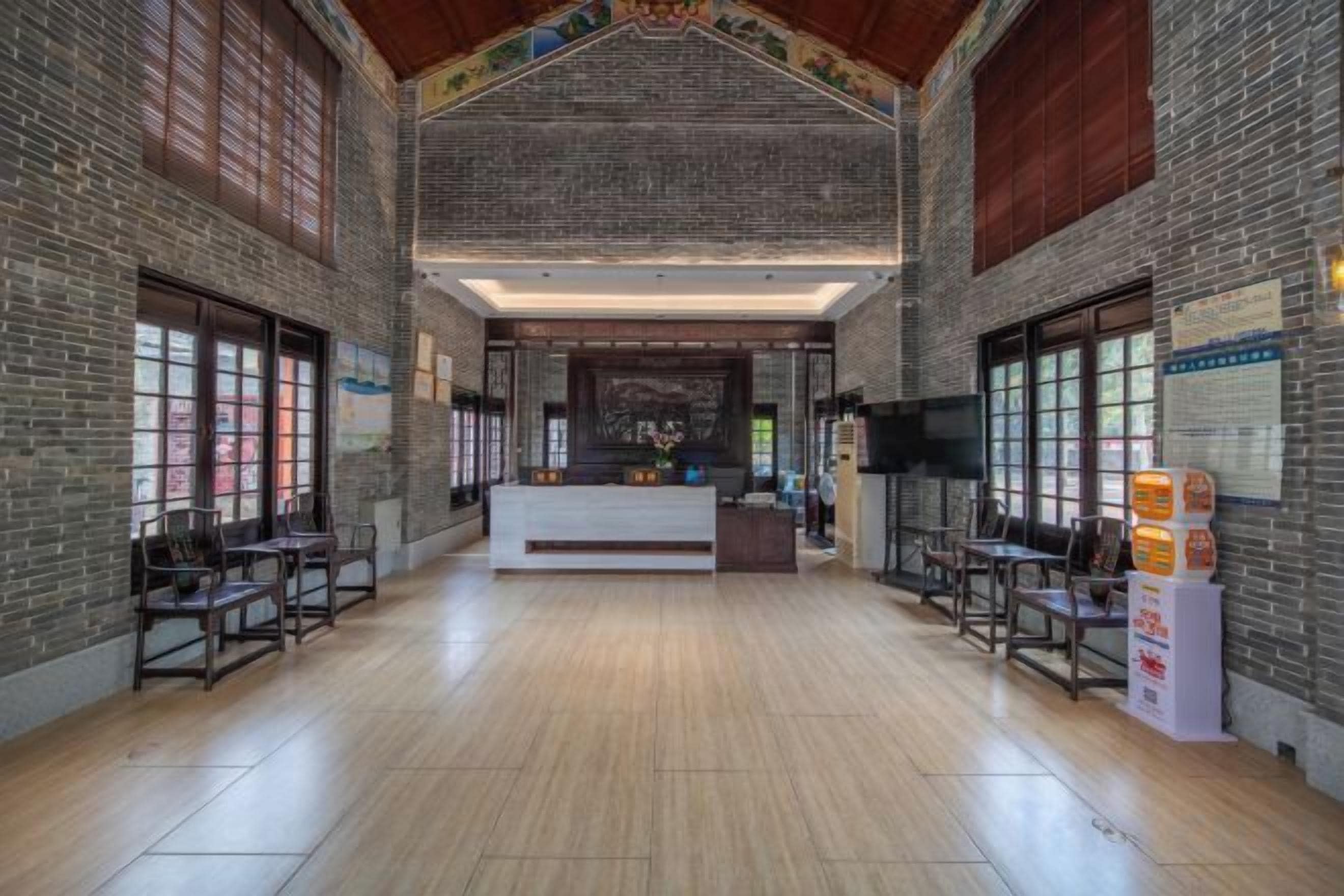 A spacious lobby with a reception desk, wooden flooring, and brick walls.