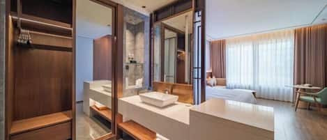 A modern hotel room with a large mirror, a wooden vanity, a bed, and a desk.