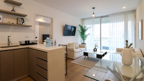 A modern living room with a glass coffee table, a sofa, and a TV mounted on the wall.