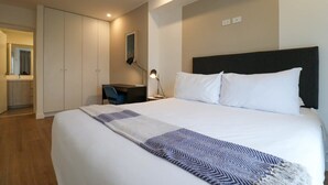 A hotel room with a large bed, a desk, a chair, a wardrobe, and a mirror.
