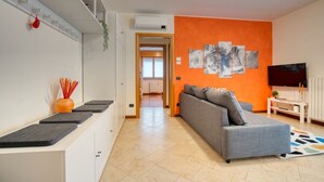 Una sala de estar moderna con un sofá gris, un televisor y una pared de acento naranja brillante.