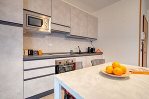 A modern kitchen with a microwave, oven, and sink. There are oranges on the counter and a coffee machine.