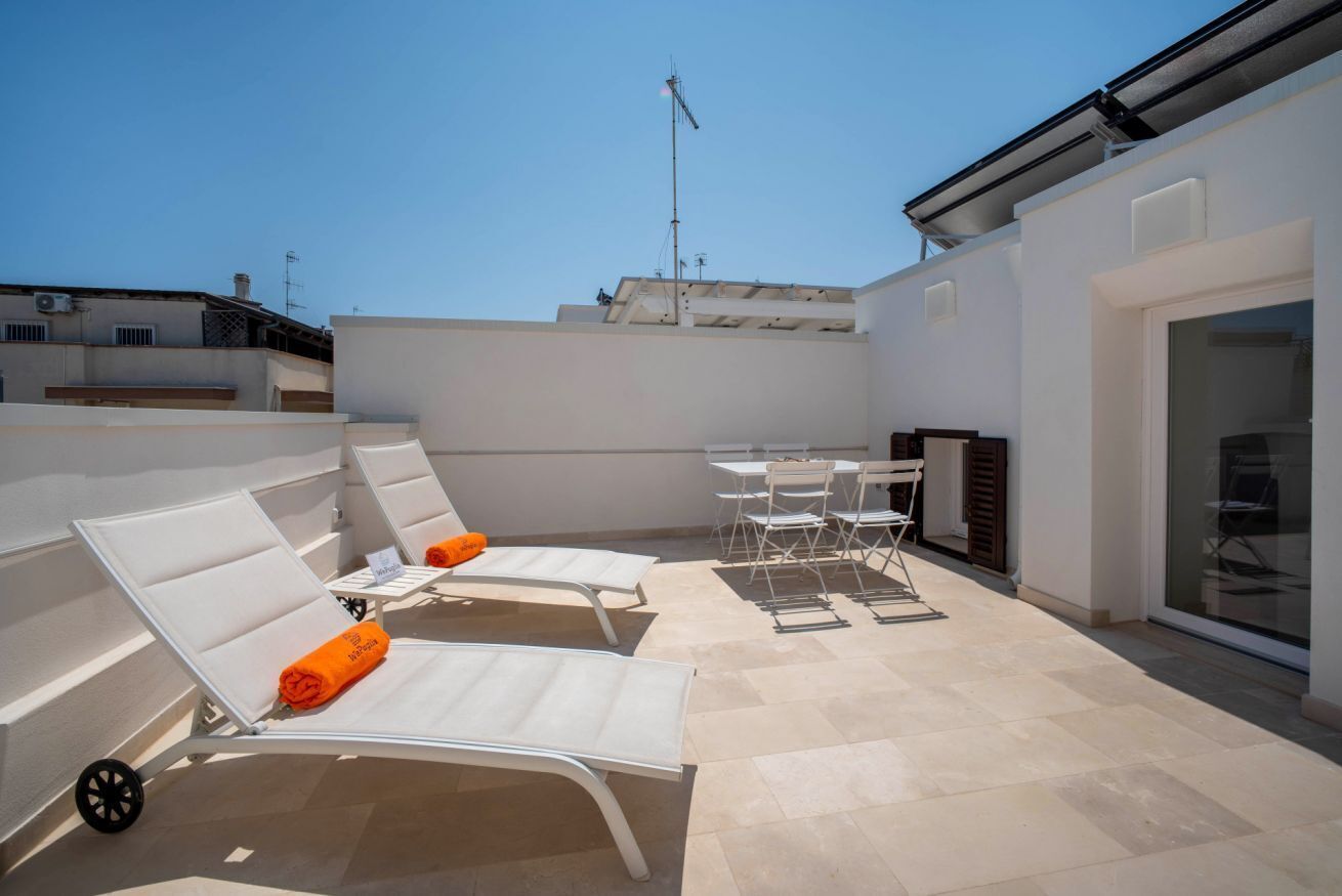 A rooftop terrace with white lounge chairs, a table, and chairs.