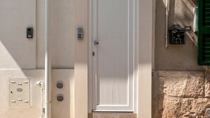 Una puerta blanca con pomo, una rejilla de ventilación y un pequeño cuadro eléctrico en la pared.