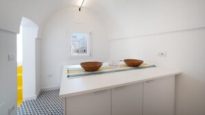 Una cocina moderna con encimera blanca, dos cestas tejidas, un felpudo a rayas y un ventanal con vistas.