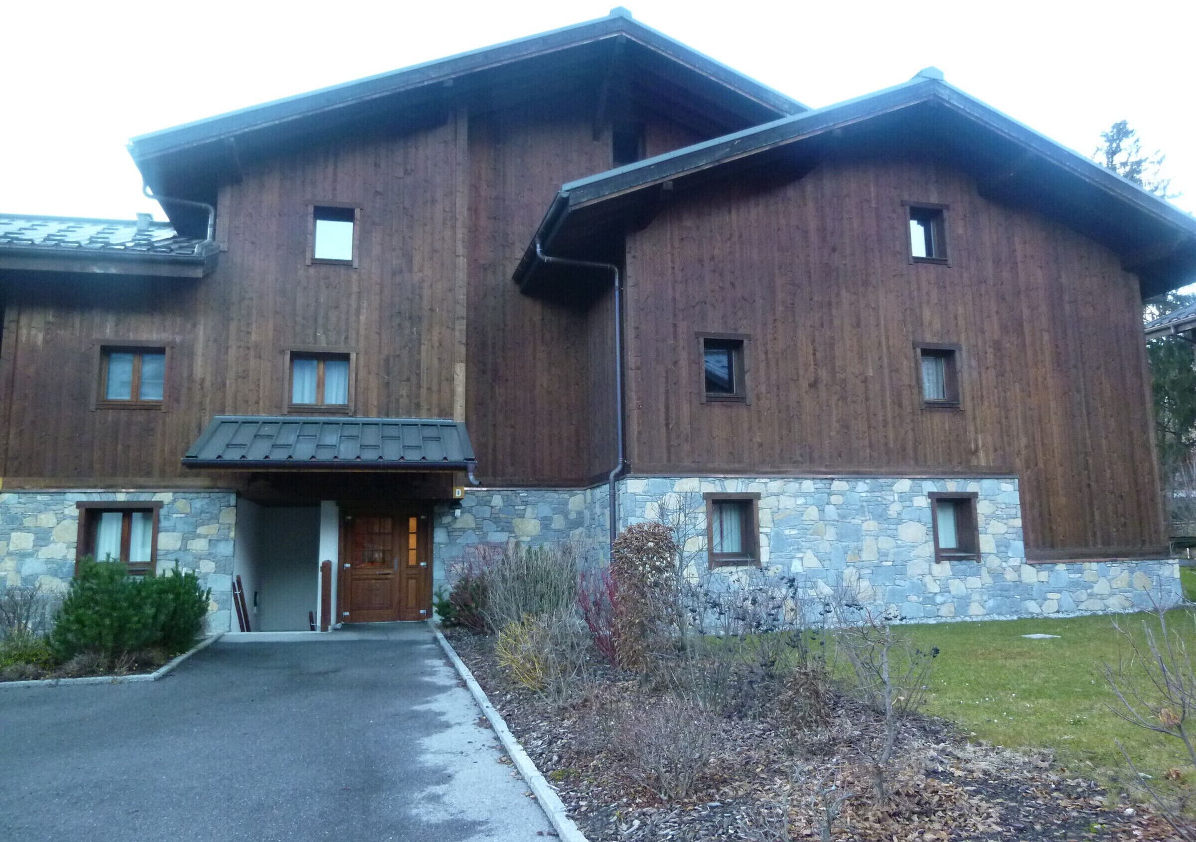 A two-story wooden building with a stone foundation, a front entrance, and a small porch area.