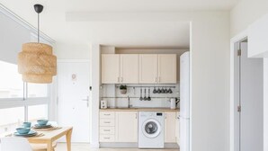 A modern kitchen with light-colored cabinets, a washing machine, and a dining area with a table and chairs.
