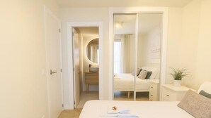 A modern bedroom with a large bed, a bedside table, a mirror, and a walk-in closet.