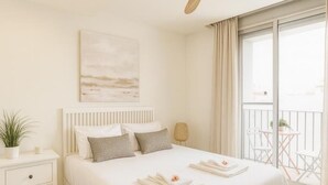A modern bedroom with a large bed, a bedside table, a small table with chairs, and a balcony with a view.