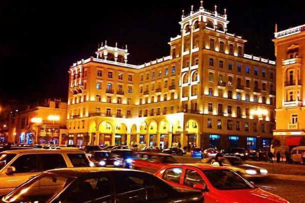 A large, historic building with multiple floors and a prominent central tower, surrounded by busy streets and parked cars.