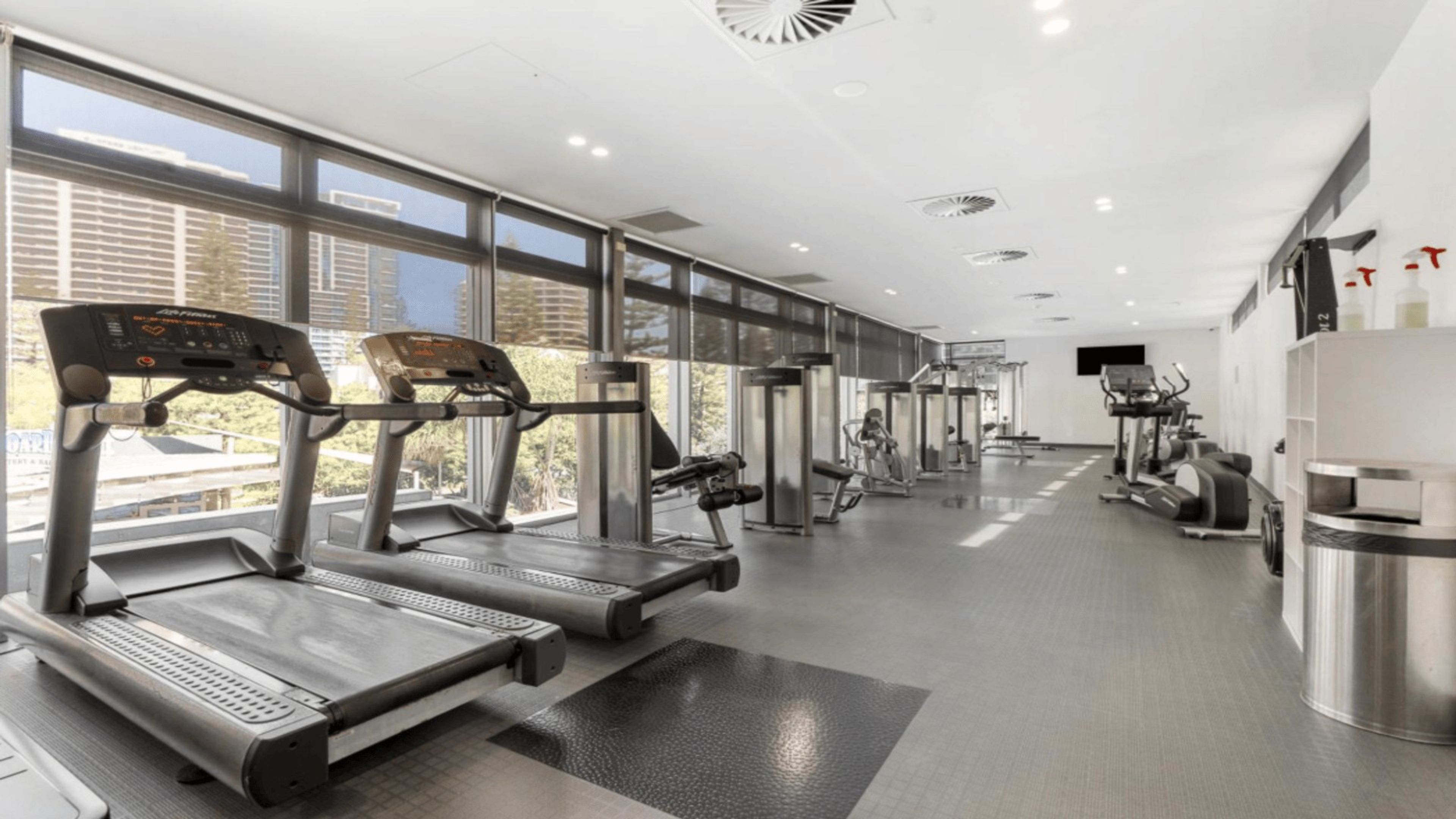 A modern gym with treadmills, weight machines, and a large window providing natural light.