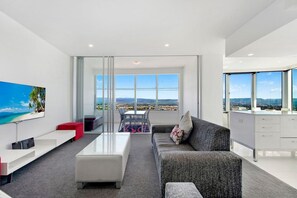 A modern living room with a large window, a flat-screen TV, a sofa, a coffee table, and a dining area. - Stunning 2 Bedroom Ocean Views Apartment (Surfers Paradise)