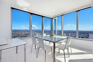 Ein moderner Essbereich mit einem Glastisch und Stühlen, große Fenster mit Blick auf die Stadt.